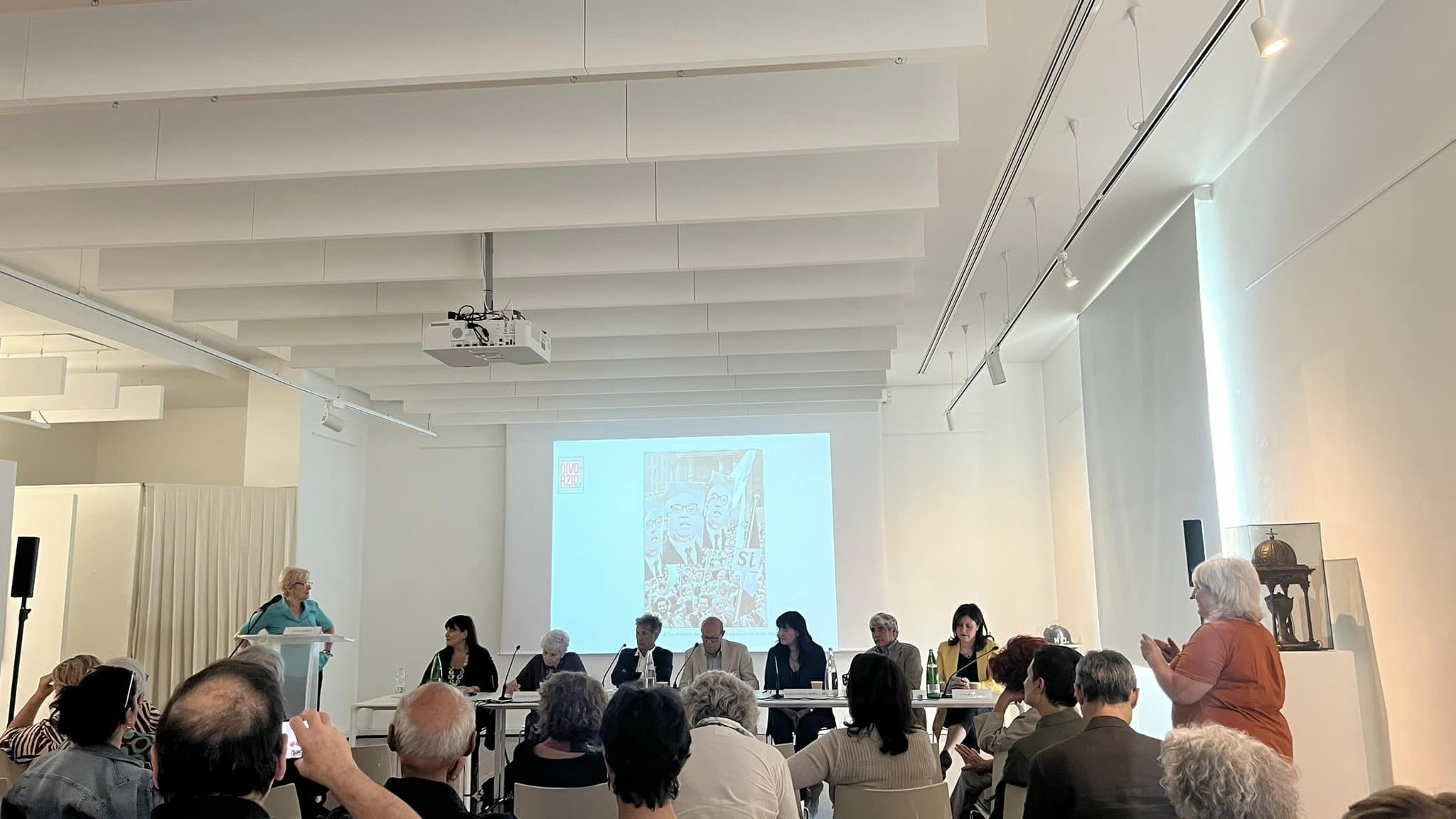 La sala dell'evento con inquadratura dal pubblico. Sul fondo il tavolo dei relatori